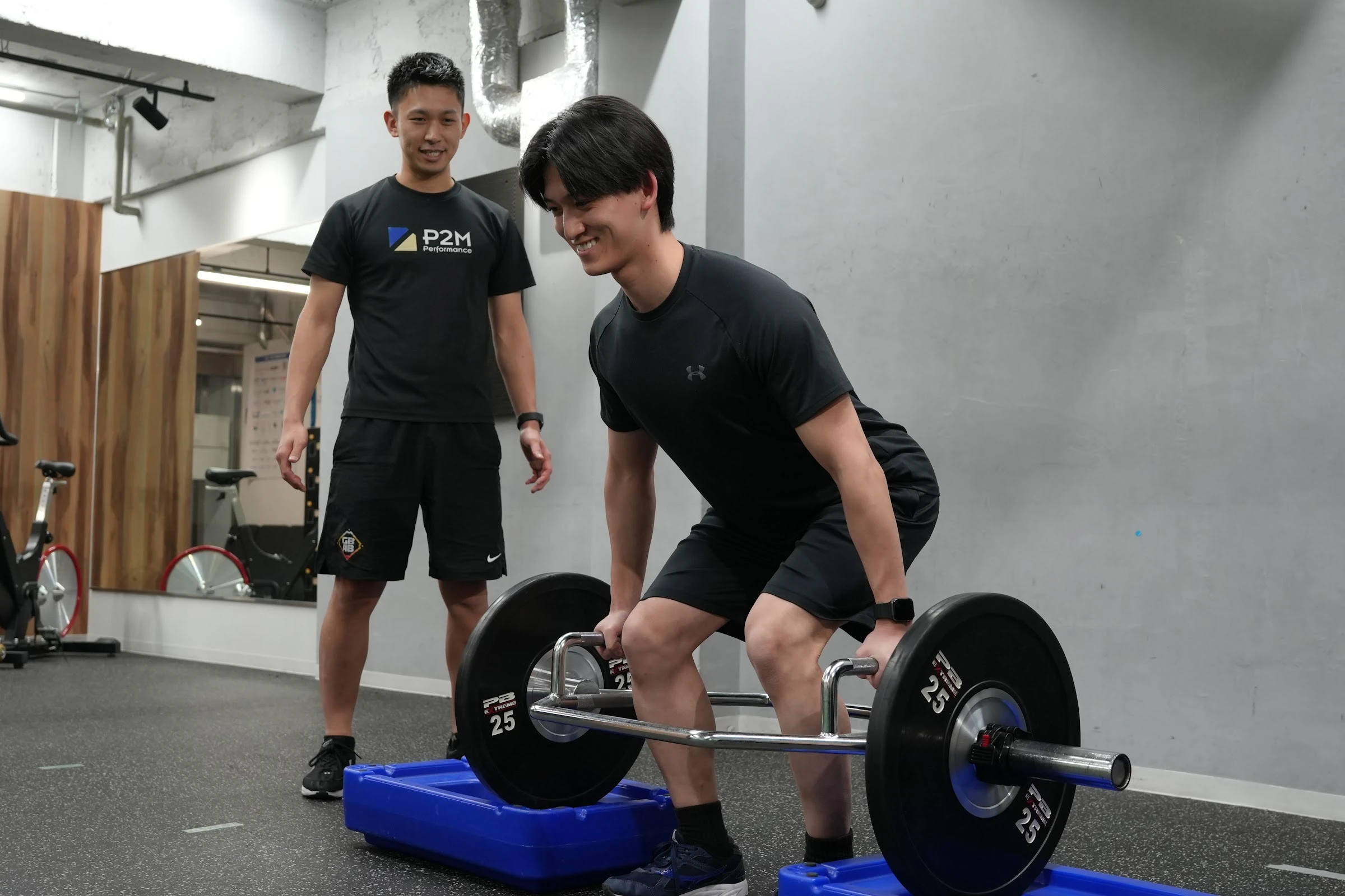 コーチが見守る中、バーベルを使ってトレーニングする利用者